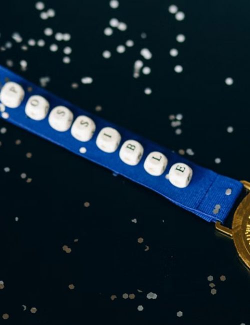 Close-up of a gold medal on a blue ribbon with 'possible' beading, symbolizing achievement.